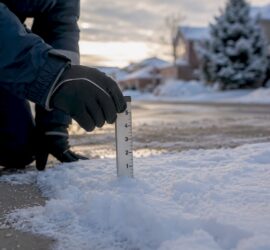 Technician measuring snow depth on parking lot stake