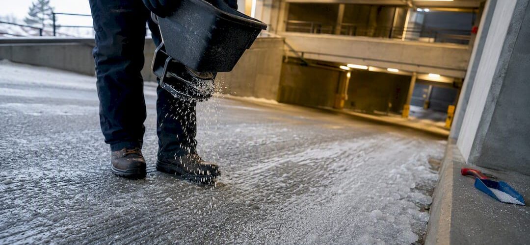 Worker applying deicer on garage ramp