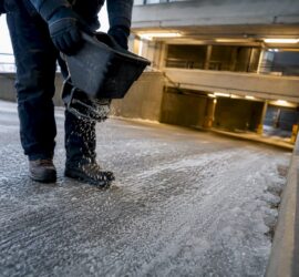 Worker applying deicer on garage ramp