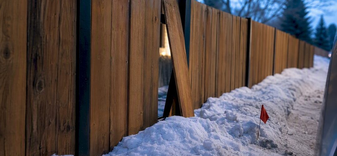 Snow-damaged residential fence beside plowed berm