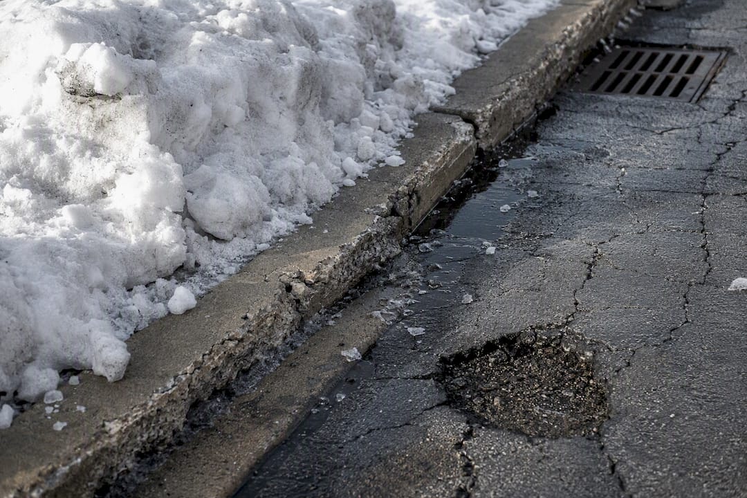 Meltwater from snow pile entering asphalt cracks
