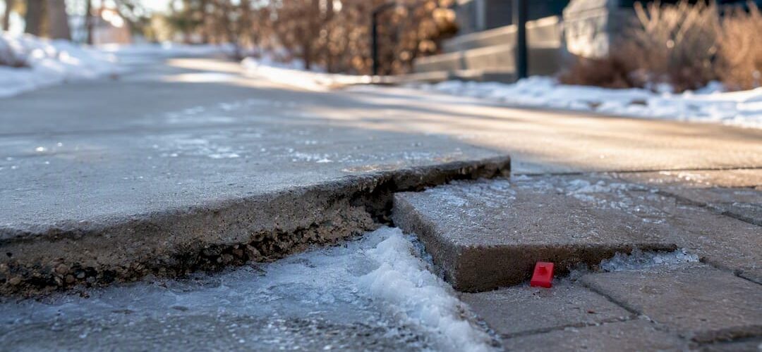 Uneven icy sidewalk with raised concrete slab